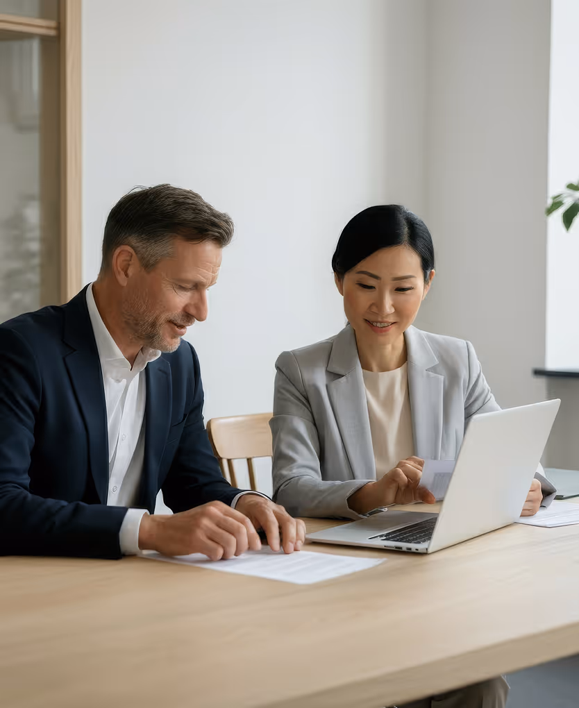 Man and woman in business attire working together at a table with laptop and documents.