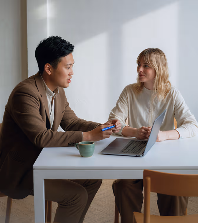 Two professionals having a discussion at a table with a laptop and coffee cup.