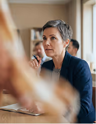Professional woman in blazer speaking and gesturing during a meeting in an office setting.
