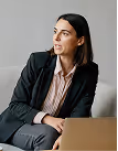 Woman in business attire sitting on a couch, looking to the side, with a laptop in front of her.