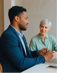 Businessman and businesswoman having a discussion across a white table.