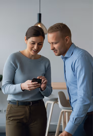 Two colleagues smiling and looking at a smartphone together in a modern office setting.