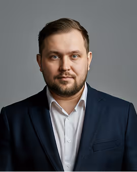 Headshot of a man with short brown hair and beard wearing a navy suit and white shirt.