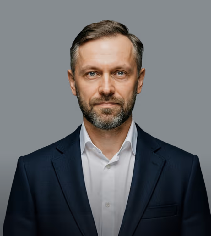 Middle-aged man with graying beard wearing a dark suit jacket and white shirt against black background.