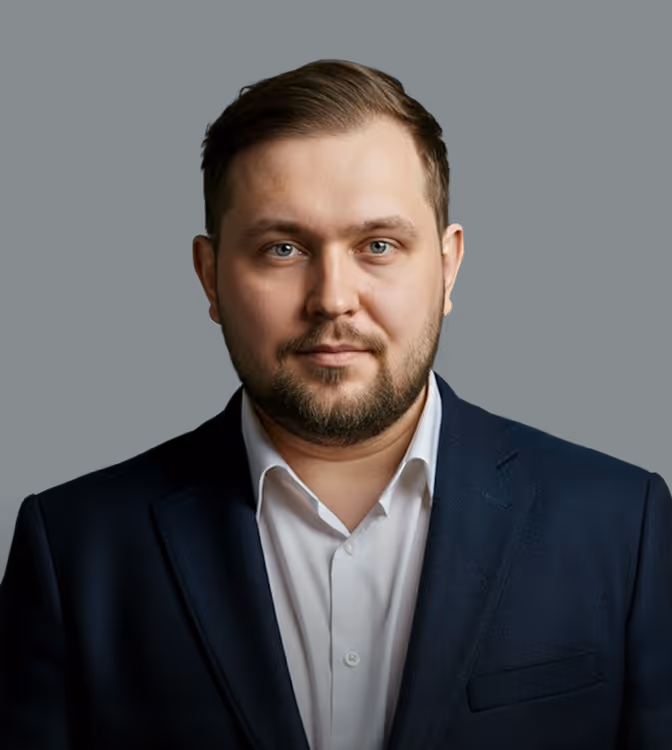 Portrait of a man with short hair and beard wearing a white shirt and dark blazer against black background.