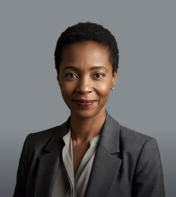 Confident woman wearing a gray blazer and white blouse against a dark background.