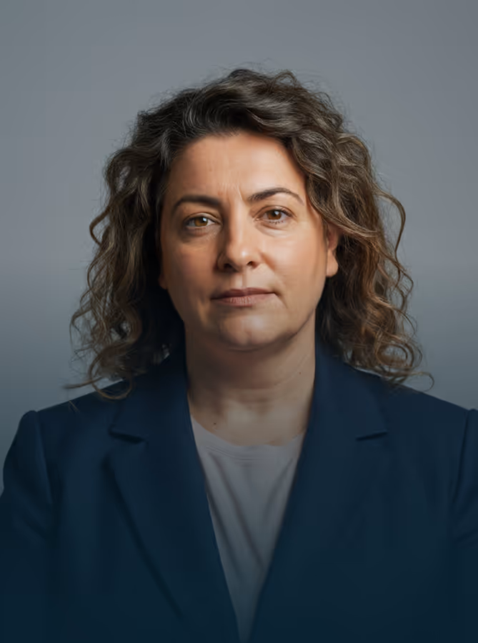 Woman with curly hair wearing a navy blazer and light shirt against a gray background.