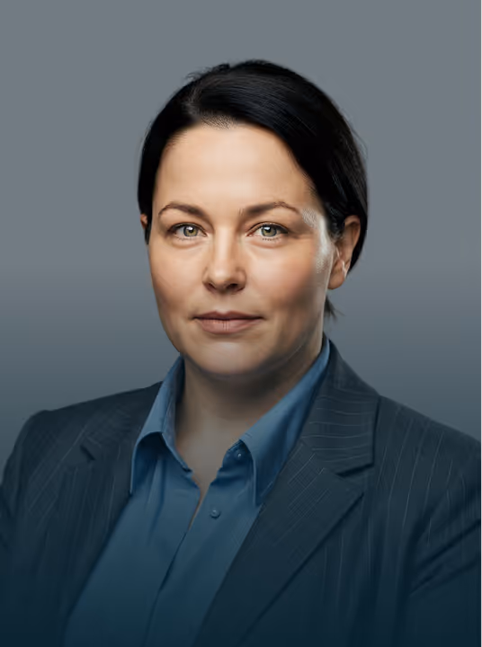 Professional woman with dark hair wearing a blue shirt and dark pinstripe blazer on gray background.